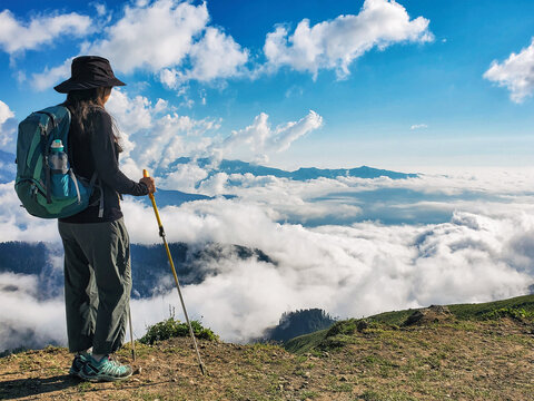 Young active woman with backpack hiking at cloudscape and mountains background