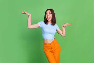 Portrait of charming crazy lady look arms palms hold empty space vs scales isolated on green color...