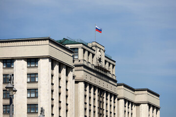 Parliament building in Moscow with Russian flag on background of blue sky. Facade of State Duma of...