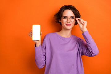 Naklejka premium Photo of confident charming girl dressed purple pullover arm eyewear showing modern gadget empty space isolated orange color background