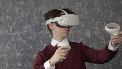A teenager wearing virtual reality glasses. A young man of Caucasian nationality , dressed in a virtual reality headset, on a gray background.
