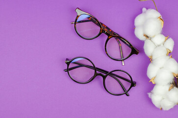 Stylish women's glasses on a purple background with cotton flowers