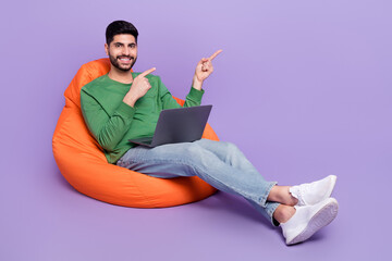 Full body photo of young latin arab man sit beanbag laptop point empty space wear stylish green...
