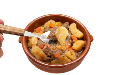 A spoonful and a clay bowl with hungarian goulash, beef, pork stew with potatoes, isolated on white background. It is a spicy dish, made mainly with meat, onions, peppers and paprika.