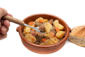 A spoonful and a clay bowl with hungarian goulash, beef, pork stew with potatoes, isolated on white background. It is a spicy dish, made mainly with meat, onions, peppers and paprika.