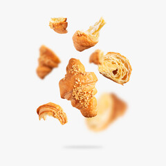 Flying whole and broken fresh croissant with butter cream isolated on light gray background. Creative bakery food background, croissant sprinkled with nuts. Sweet pastry, bun, dessert, confectionery