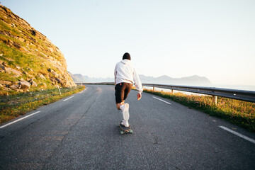Hipster skater ride on longboard on empty epic road. Millennial man in hoodie and shorts ride...