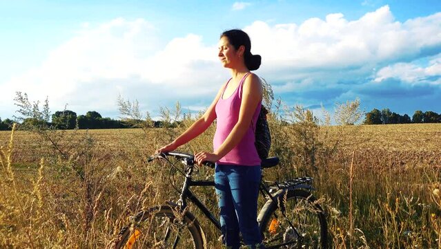 Young happy woman on a bike in the field. Girl rides a bike in nature. Close-up portrait, view from behind the grass. Camera movement.Concept of happiness, recreation, sports, nature.