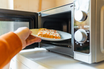 Uncooked frozen small pizza placed into the microwave.junk food,fast food concept.Side view.Selective focus.