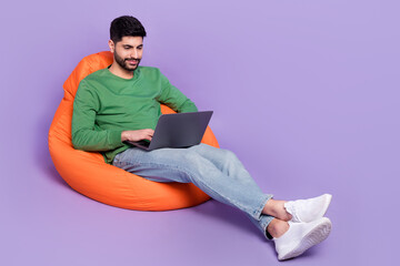 Full body photo of young latin guy sitting coding new software entrepreneur wear stylish green garment isolated on purple color background