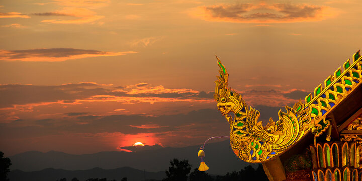 Beautiful golden naga and buddhist bells hanging on art roof of buddhist temple,Gable of the Thai Northern art style, Buddhist temple with sunset. in Temple at Chiang Mai 