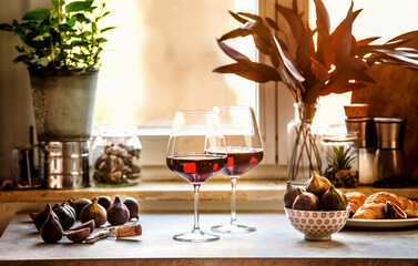 Two glasses red wine on kitchen table with figs at window background. Front view