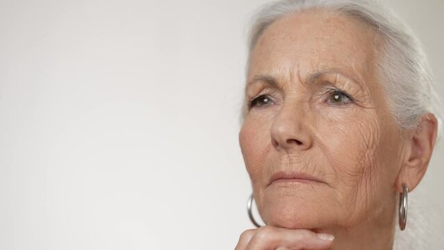 A close-up view of a calm old mature woman with gray hair looking to side isolated on solid white background in studio