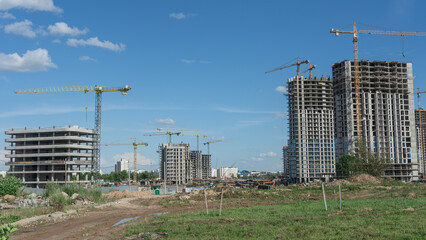 Construction of a multi-story residential buildings. Defocused foreground with young tree. Cranes work. Construction site.
