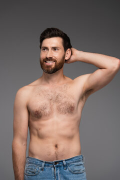 shirtless and bearded man looking away while smiling isolated on grey.
