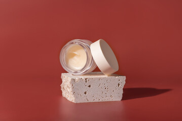 Glass Cosmetic jar on travertine stones on red close up. Skincare beauty product