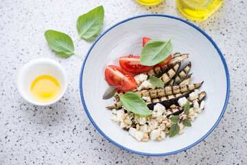 Salad with grilled eggplant and cheese served in a blue and white plate, elevated view on a light-grey granite background