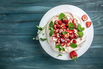 Homemade delicious meringue cake Pavlova with whipped cream, fresh strawberries and mint on wooden...