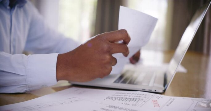 Man paying bills, doing financial planning on a laptop at home. Closeup of male hands checking paperwork, doing ebanking and applying for a loan to pay off his debt after losing his job during corona