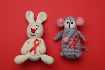 Cute knitted toys with ribbons on red background, top view. AIDS disease awareness