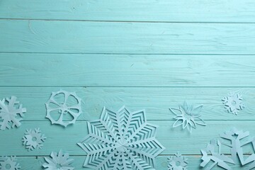 Many paper snowflakes on turquoise wooden background, flat lay. Space for text