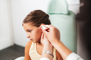Female audiologist examining girl ear using otoscope in doctors office. Child receiving a ear exam....