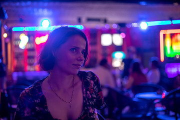 A beautiful girl sits at the bar and smiles. Portrait of a beautiful girl. Neon lights. Girl at night in a bar. Beautiful light.