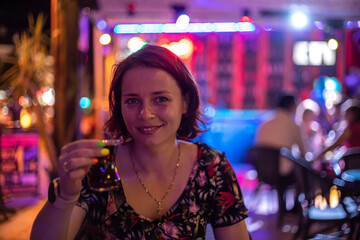 A beautiful girl sits at the bar and smiles. Portrait of a beautiful girl. Neon lights. Girl at night in a bar. Beautiful light.