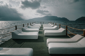 White sunbeds stand on the pier. Nice pier. Sea coast. Mountains in the background. Beautiful...