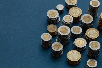Piles of Mexican pesos coins arranged in the corner of the image with copy space and a blue background