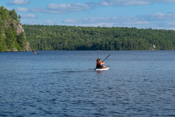 Young fit woman in a life jacket in a kayak paddling on a lake surrounded by high rocky cliffs and...