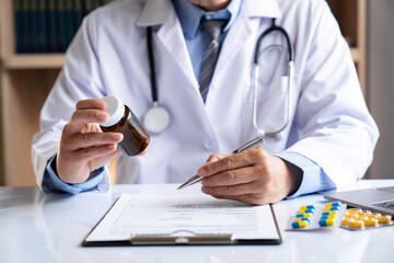male medicine doctor hand holds the bottle of pills and writes a prescription to the patient at the...