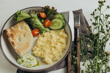 Breakfast of scrambled eggs, bread and vegetables