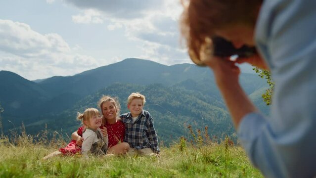 Father taking photos family sitting grass mountain meadow. People enjoy summer.