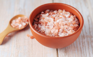 A wooden spoon and a ceramic bowl with pink Himalayan salt