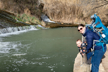 Mother and son with the baby carrier looking at camera and smiling in front of the river in the valley of Alcalá del Júcar - Albacete Province