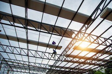 Construction workers wearing yellow plastic helmets and seat belts are installing the factory roof...