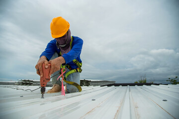 Construction workers wearing yellow plastic helmets and seat belts are installing the factory roof...