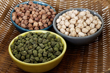 Assortment of dry chickpea piles in bowls. Three different chick pea kinds: green, kala chana and white.