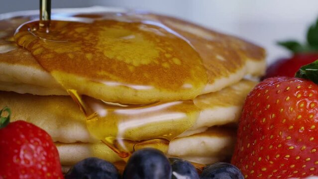 Close up shot of maple syrup being poured over warm stacked pancakes and fruit, in slow motion