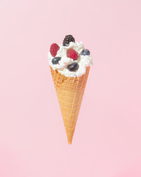 Ice cream cone with cream and blueberries, raspberries and blackberries. Pastel background. Minimal summer fruit concept.