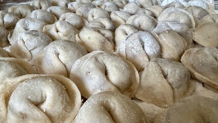  Sculpts dumplings and puts them on a wooden table, there are a lot of them, they are appetizing in flour and waiting to be cooked Each dumpling is full of meat, they are round and neatly handmade