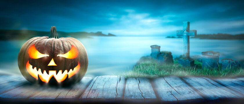 One spooky halloween pumpkin, Jack O Lantern, with an evil face and eyes on a rustic wooden bench, table with a misty blue night coastal background with space for product placement.