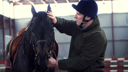close-up, in a stable, a man strokes a muzzle of a thoroughbred, black horse