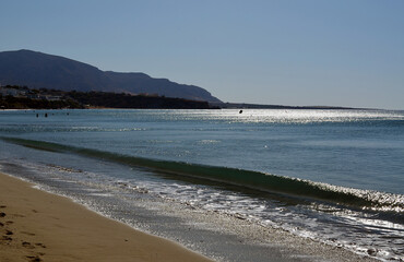 Waves are rolling onto the sandy beach against the background of distant mountains. Makry Gialos, Crete Island, Greece.