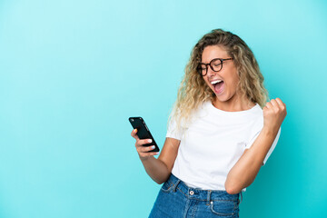 Girl with curly hair isolated on blue background with phone in victory position