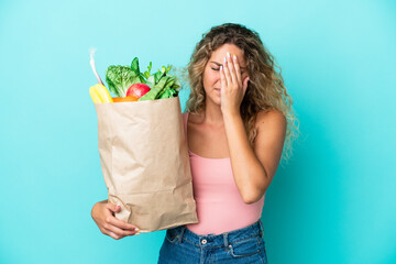 Girl with curly hair holding a grocery shopping bag isolated on green background with tired and sick expression