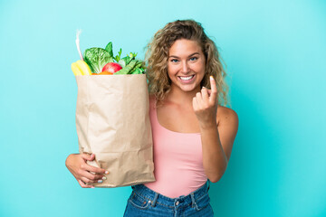 Girl with curly hair holding a grocery shopping bag isolated on green background doing coming gesture