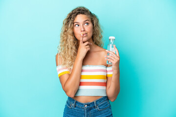 Young blonde woman with a bottle of water isolated on blue background having doubts while looking up