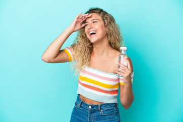 Young blonde woman with a bottle of water isolated on blue background smiling a lot